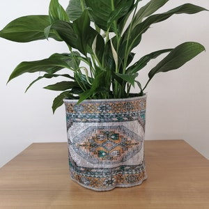 May include: A peace lily plant in a decorative pot with a colourful patterned design. The pot is made of fabric and has a scalloped edge.