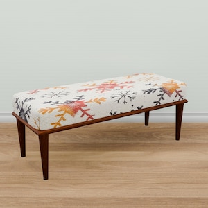 May include: A white bench with a snowflake pattern on the cushion. The bench has wooden legs and is sitting on a wooden floor.