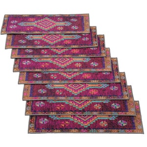May include: A set of eight colourful patterned rugs with a geometric design. The rugs are stacked on top of each other, with the top rug being the most visible. The rugs are a mix of pink, purple, blue, and orange.