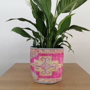 May include: A peace lily plant in a pink and yellow patterned fabric planter. The planter has a light gray border.