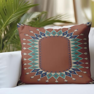 Puede incluir: Un cojín decorativo con un diseño geométrico. El cojín presenta un fondo de color óxido con una forma rectangular central. El borde está adornado con patrones de diamantes y zigzags azules, turquesas y blancos. Se ve otro cojín marrón.