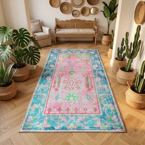 May include: A rectangular, vintage-style rug with a pink central field and a turquoise border. The rug features intricate floral and geometric patterns in shades of pink, green, and turquoise, adding a touch of bohemian flair to any room.