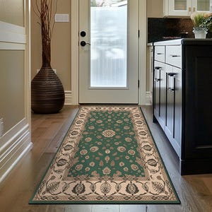 以下が含まれることがあります： 緑とベージュの長方形の柄のラグ。廊下の木製の床に敷かれています。ラグは、花のモチーフとベージュのボーダーが付いた緑色の中心部を持っています。