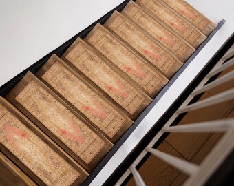 May include: A set of eight stair treads with a patterned design in shades of brown, beige, and red. The treads are made of a woven material and have a fringed edge.