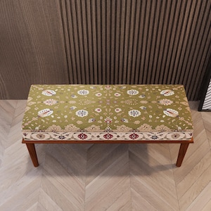 Puede incluir: Un banco rectangular con una parte superior verde estampada y un marco de madera. La tela presenta un diseño floral en blanco, rojo y azul. El banco tiene cuatro patas de madera en ángulo.