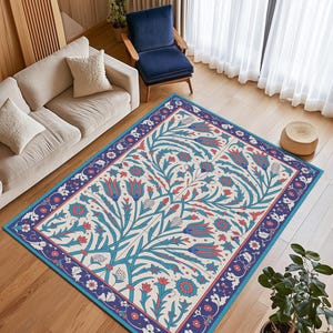 Puede incluir: Una alfombra rectangular con un diseño floral. La alfombra presenta un fondo color crema con un patrón de flores azules y rojas y hojas verdes. El borde es azul oscuro con detalles florales.