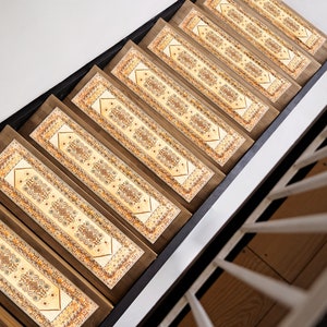 Puede incluir: Un conjunto de peldaños de escalera con estampado beige y marrón con un diseño decorativo. Los peldaños están hechos de un material similar a la madera y están diseñados para colocarse en las escaleras.