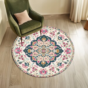 May include: A round, cream-colored rug with a colorful floral pattern. The rug has a dark blue center with pink, yellow, and green accents. The rug is on a wooden floor.
