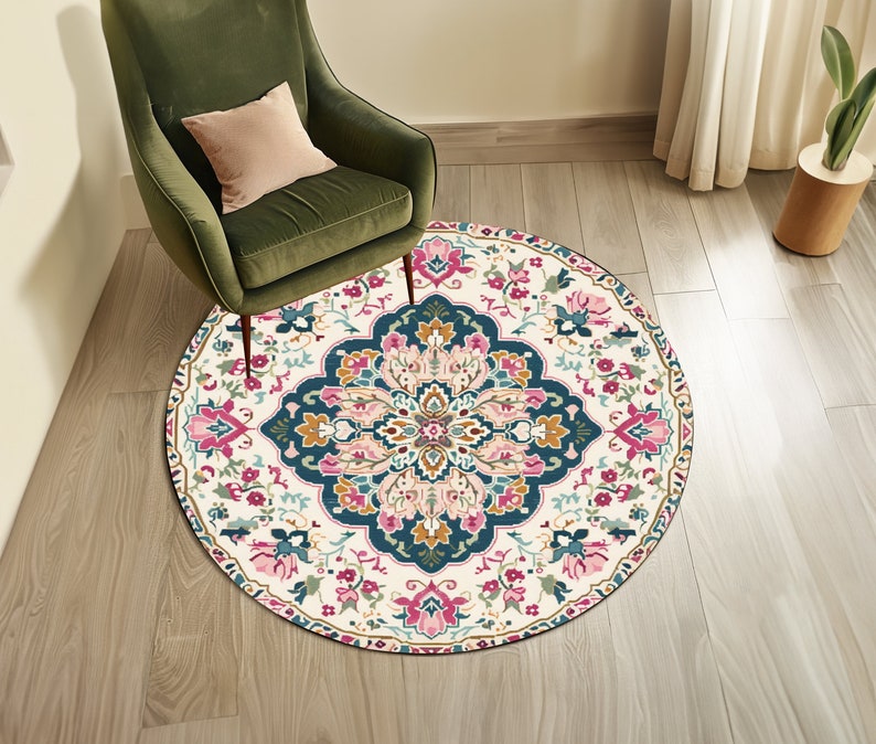 May include: A round, cream-colored rug with a colorful floral pattern. The rug has a dark blue center with pink, yellow, and green accents. The rug is on a wooden floor.
