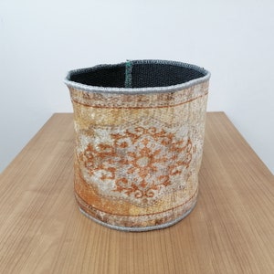 Könnte beinhalten: Ein runder, geflochtener Aufbewahrungskorb mit einem beige-braunen Muster. Der Korb hat einen grauen Rand oben.