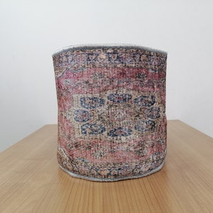 May include: A cylindrical storage basket made from a woven rug with a pink, blue, and beige pattern.