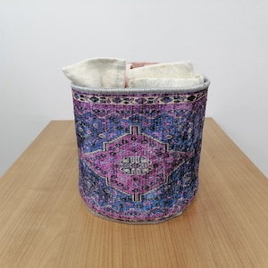 May include: A purple and blue patterned fabric storage basket with a white fabric liner. The basket is sitting on a wooden surface.