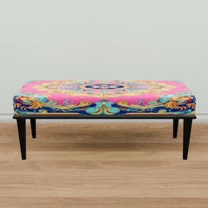 May include: A pink and blue patterned ottoman with black legs. The ottoman has a floral design with gold accents.