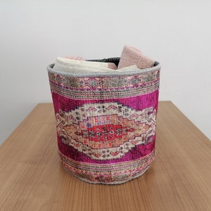May include: A pink and cream patterned fabric storage basket with a gray trim. The basket is filled with folded towels.