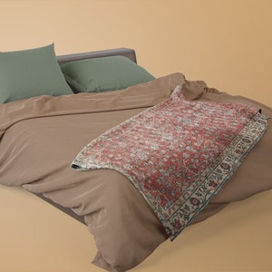 May include: A brown bed with a green pillow and a red and white patterned throw blanket.
