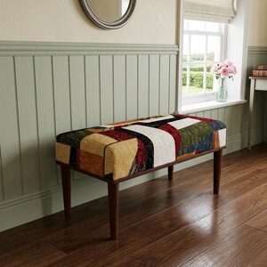 May include: A rectangular bench featuring a multi-colored fabric upholstery with a geometric patchwork pattern in shades of yellow, red, green, white, and black. The bench is supported by four tapered dark brown wooden legs.