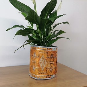May include: A peace lily plant in a yellow and white patterned fabric planter. The planter has a geometric design.
