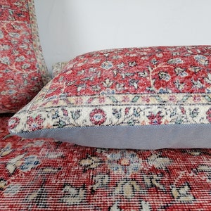 May include: Two red and cream patterned throw pillows with a floral design. The pillows have a grey backing and are made of a soft, woven fabric.