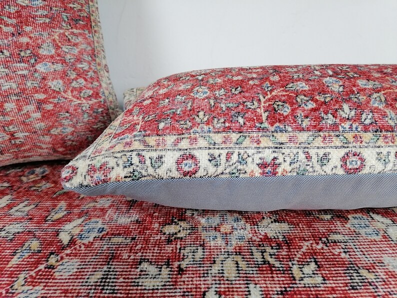 May include: Two red and cream patterned throw pillows with a floral design. The pillows have a grey backing and are made of a soft, woven fabric.