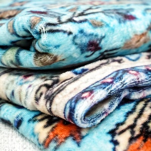 K&ouml;nnte beinhalten: Ein Stapel blauer, wei&szlig;er und orangefarbener Fleece-Decken mit Mustern. Die Decken sind gefaltet und haben eine weiche, flauschige Textur.