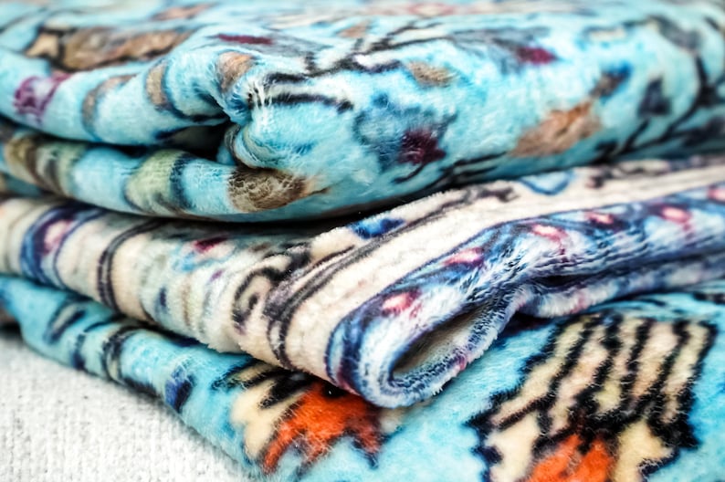 K&ouml;nnte beinhalten: Ein Stapel blauer, wei&szlig;er und orangefarbener Fleece-Decken mit Mustern. Die Decken sind gefaltet und haben eine weiche, flauschige Textur.