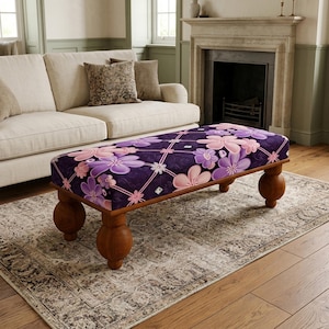 May include: A rectangular ottoman featuring a dark purple fabric upholstery with a repeating pattern of light pink and lavender flowers connected by thin pink lines. The piece stands on four rounded, dark brown wooden ball-shaped legs.