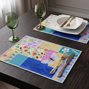 Può includere: Due tovagliette rettangolari con un design patchwork di motivi floreali, quadretti vichy gialli, pois blu e una farfalla bianca. Ogni tovaglietta è disposta con una forchetta e un coltello dorati, accompagnati da un bicchiere verde e stoviglie bianche.