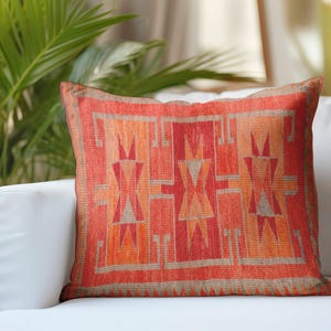 May include: A square throw pillow featuring a vibrant red and orange geometric pattern with intricate lines and triangular shapes. The design is symmetrical, showcasing a warm color palette with muted grey accents throughout the woven fabric texture.