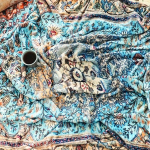 K&ouml;nnte beinhalten: Eine blaue und orangefarbene gemusterte Wolldecke mit einer Tasse Kaffee darauf.