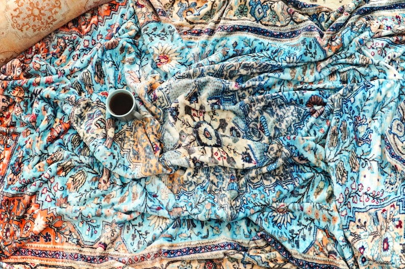 K&ouml;nnte beinhalten: Eine blaue und orangefarbene gemusterte Wolldecke mit einer Tasse Kaffee darauf.
