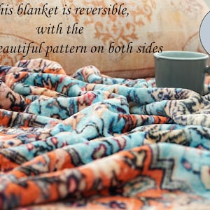 K&ouml;nnte beinhalten: Eine blaue und orangefarbene Fleece-Decke mit dem Text "This blanket is reversible, with the same beautiful pattern on both sides" und "SAMPLE" auf dem Bild.