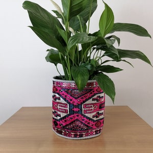 May include: A peace lily plant in a pink and white patterned fabric planter. The planter has a geometric design with a black outline.