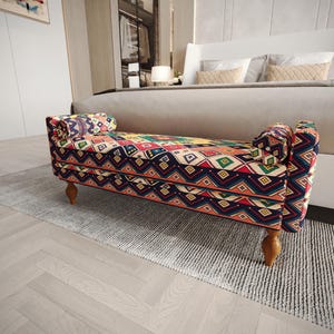 May include: A rectangular upholstered bench featuring a vibrant, multi-colored geometric pattern with diamonds and stripes in shades of red, blue, green, and yellow. The bench has two cylindrical bolster pillows at each end and four wooden legs.