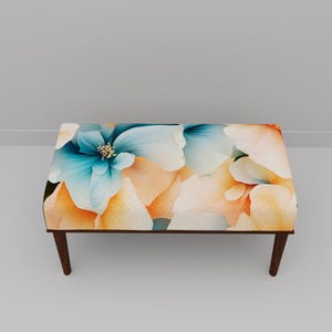 May include: Rectangular ottoman with a floral pattern in shades of blue, peach, and white. The flowers are large and detailed, with a dark brown wooden frame and legs. The ottoman is approximately 36 inches long, 18 inches wide, and 16 inches high.