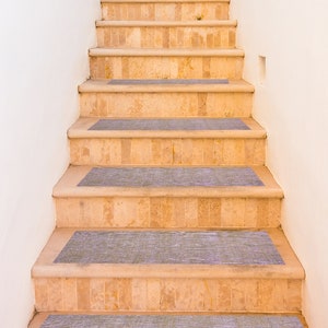 Könnte beinhalten: Eine Treppe aus beigefarbenem Stein mit grauen, rutschfesten Stufen. Die Treppe befindet sich an einer weißen Wand.