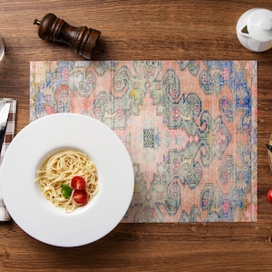 Peut inclure: Une assiette blanche avec une portion de spaghetti garnie de tomates cerises et d'une feuille de basilic, posée sur un set de table à motifs colorés. Le set de table est sur une table en bois avec un verre d'eau, un pot de sel et de poivre, un petit pot à crème blanc, une bouteille d'huile d'olive et une planche à découper en bois avec des tomates cerises.