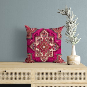 May include: A pink throw pillow with a colorful geometric pattern. The pillow is sitting on a wooden shelf with a vase and a plant.