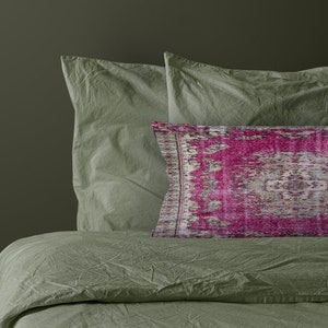 May include: A green bed with two green pillows and a pink patterned pillow. The bed is made with a soft, crinkled fabric.