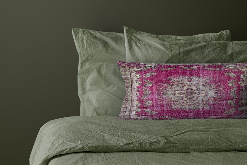 May include: A green bed with two green pillows and a pink patterned pillow. The bed is made with a soft, crinkled fabric.