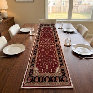 May include: A rectangular table runner featuring a deep red central field with intricate floral patterns in cream and gold, framed by a wide black border with repeating ornate motifs, laid flat along the center of a dark wooden dining table.