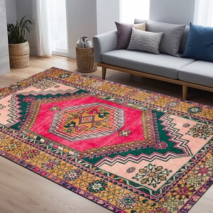 Op de afbeelding: Een kleurrijk vintage tapijt met een geometrisch patroon in roze, groen en geel. Het tapijt heeft een traditioneel ontwerp met ingewikkelde details en een verweerde uitstraling.