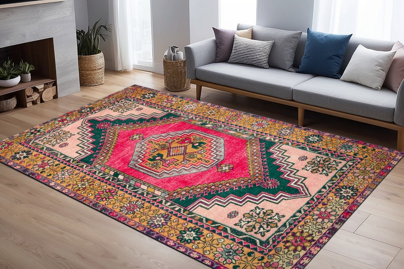 Op de afbeelding: Een kleurrijk vintage tapijt met een geometrisch patroon in roze, groen en geel. Het tapijt heeft een traditioneel ontwerp met ingewikkelde details en een verweerde uitstraling.