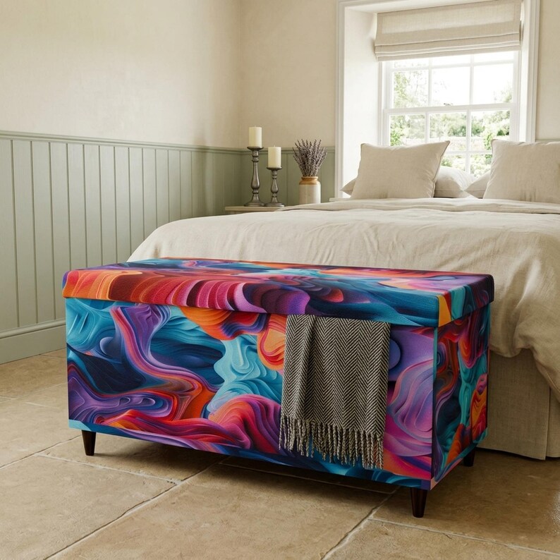a bedroom with a colorful, abstract-patterned storage bench or ottoman in the foreground, and a bed with white bedding and pillows in the background.