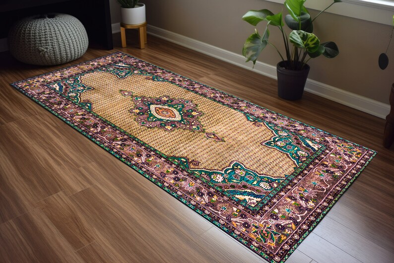 May include: A long, rectangular rug with a beige background and a colorful floral pattern. The rug has a teal, pink, and green border with intricate details.