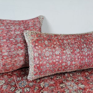 May include: Two red and cream patterned throw pillows with a floral design. The pillows are on a red and cream patterned rug.