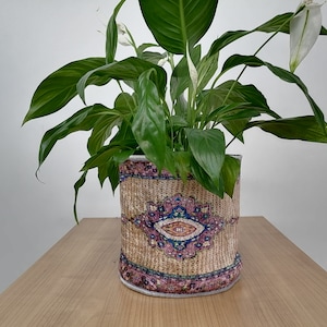 Peut inclure: Un plant de spathiphyllum dans un pot décoratif avec un motif coloré. Le pot est en matériau tissé et présente un motif brun, rose et bleu.