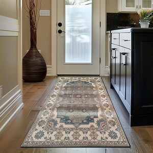 Puede incluir: Una alfombra rectangular con un patrón floral y geométrico en tonos azules, beige y grises. La alfombra está colocada sobre un suelo de madera en un pasillo, con una puerta y armarios de cocina visibles en el fondo.