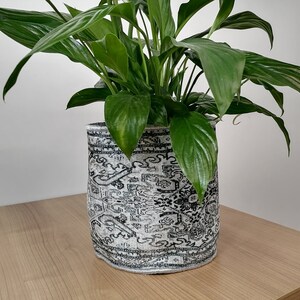 Op de afbeelding: Een groene vredeslelie in een witte keramische pot met een zwart-wit patroon.