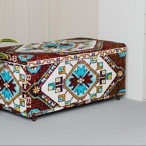 May include: A rectangular storage ottoman with a patterned fabric design. The pattern features geometric shapes in shades of brown, white, blue, and yellow. The ottoman has short, dark wooden legs and a hinged lid.