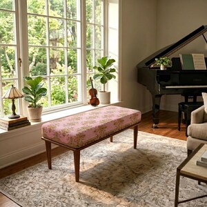 A cozy living room with a grand piano, a pink bench, and a large window overlooking a lush garden.